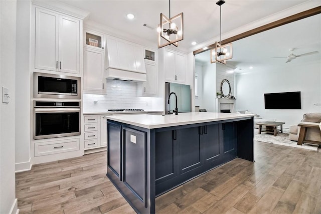 kitchen with ceiling fan with notable chandelier, stainless steel appliances, pendant lighting, white cabinets, and light hardwood / wood-style floors