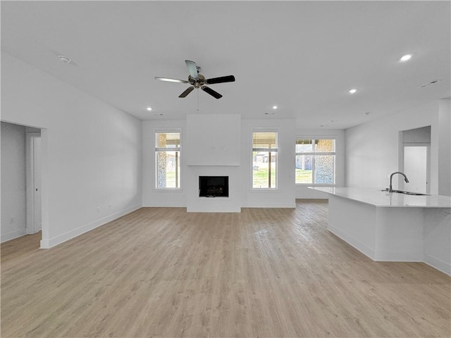 unfurnished living room featuring ceiling fan, sink, and light wood-type flooring