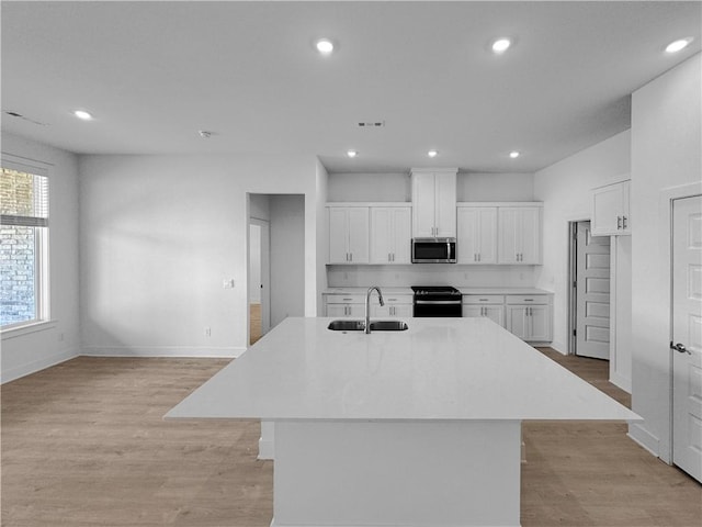 kitchen featuring a center island with sink, white cabinetry, electric range, and sink