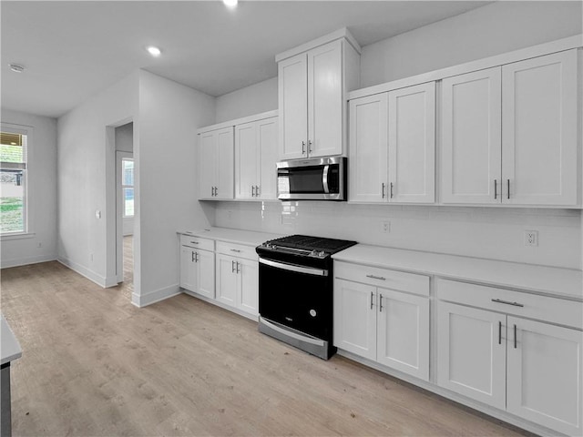 kitchen with white cabinets, appliances with stainless steel finishes, backsplash, and light hardwood / wood-style flooring