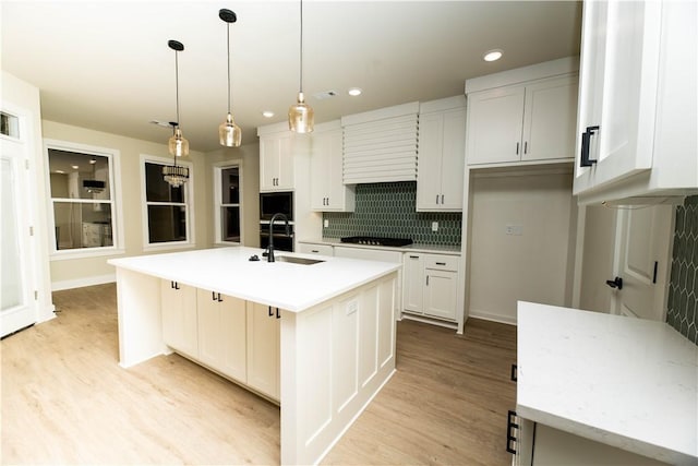 kitchen featuring backsplash, a center island with sink, white cabinets, and hanging light fixtures