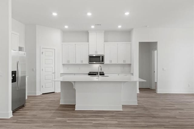 kitchen with white cabinets, stainless steel appliances, a kitchen island with sink, and light hardwood / wood-style floors