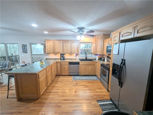 kitchen with light brown cabinetry, a breakfast bar, stainless steel appliances, sink, and light hardwood / wood-style flooring