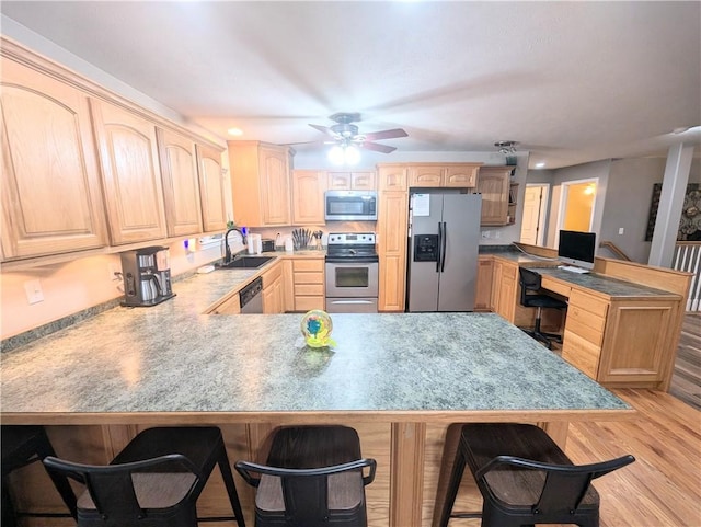 kitchen featuring a breakfast bar area, light hardwood / wood-style flooring, light brown cabinetry, kitchen peninsula, and stainless steel appliances