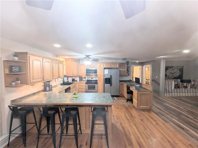 kitchen featuring light brown cabinets, light wood-type flooring, a kitchen bar, kitchen peninsula, and stainless steel appliances