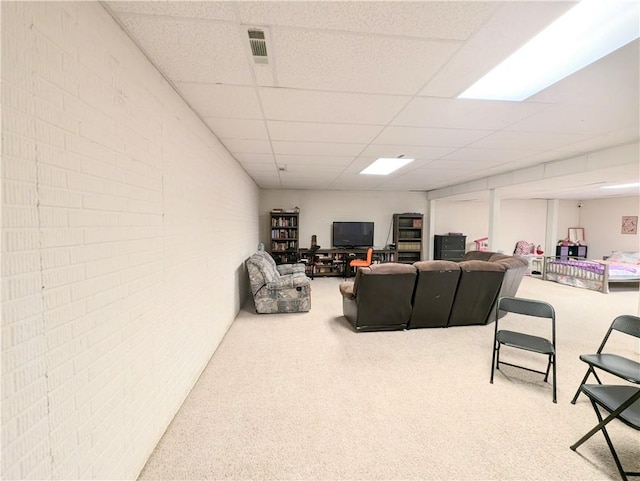 carpeted living room with a drop ceiling and brick wall