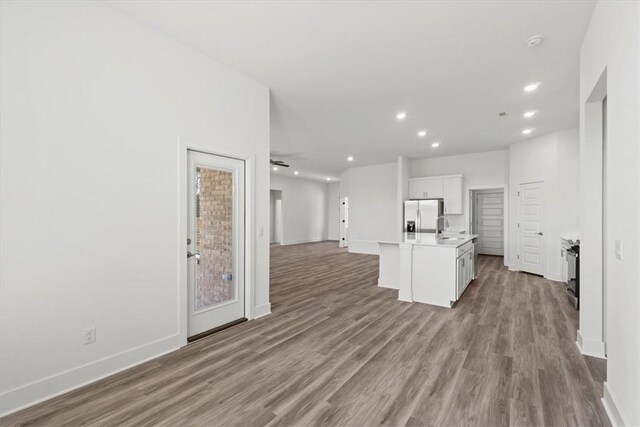 kitchen featuring sink, light hardwood / wood-style flooring, stainless steel fridge, an island with sink, and white cabinetry