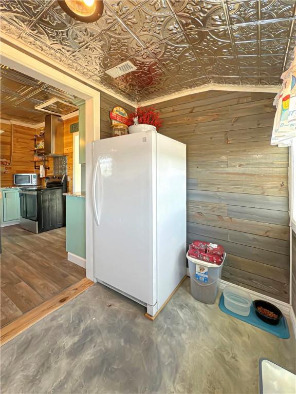 kitchen featuring wall chimney exhaust hood, wood walls, lofted ceiling, and stainless steel appliances