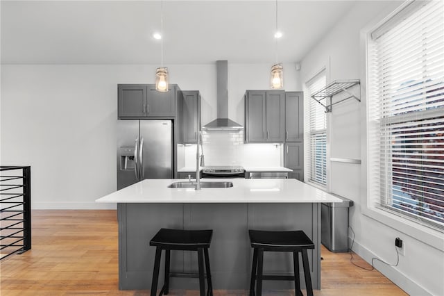 kitchen with gray cabinetry, light wood-type flooring, wall chimney range hood, and stainless steel refrigerator with ice dispenser