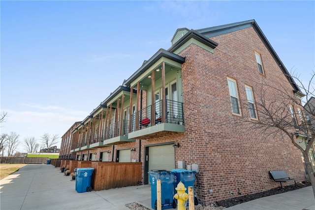 view of side of home with driveway, brick siding, an attached garage, and a balcony