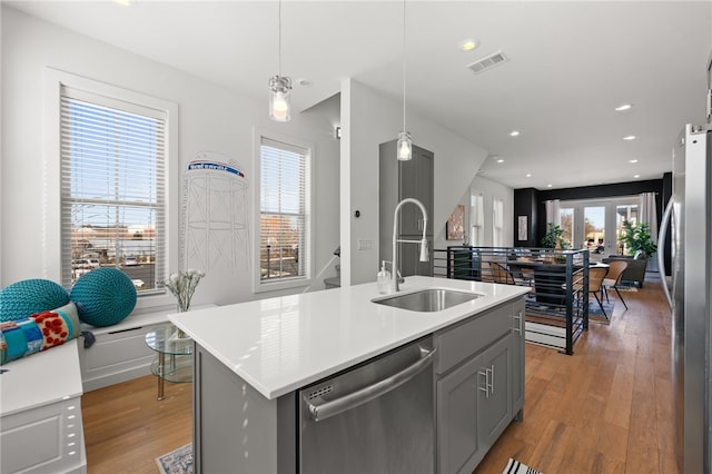 kitchen with gray cabinetry, stainless steel appliances, a sink, light countertops, and light wood-type flooring