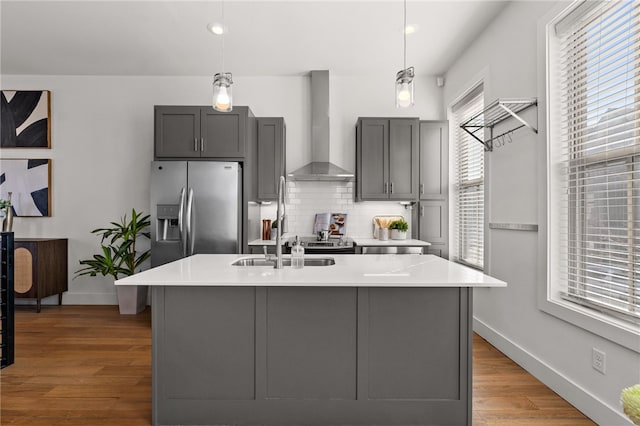 kitchen featuring wall chimney exhaust hood, tasteful backsplash, stainless steel refrigerator with ice dispenser, and gray cabinets