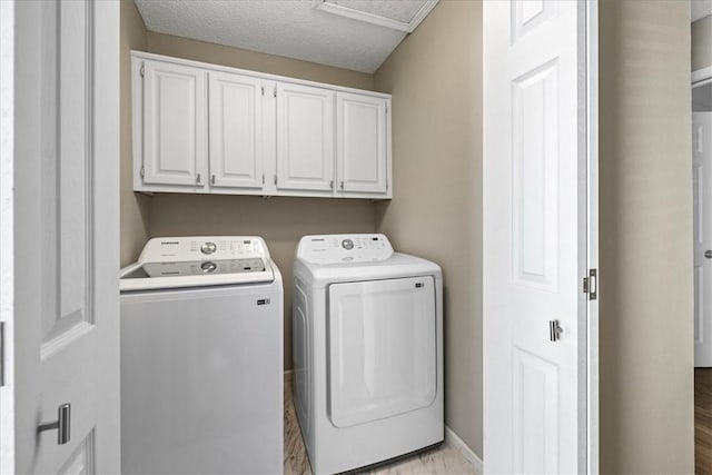 washroom featuring washer and dryer, light hardwood / wood-style floors, cabinets, and a textured ceiling