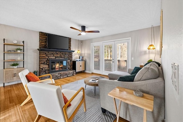 living room featuring hardwood / wood-style floors, ceiling fan, a stone fireplace, and a textured ceiling