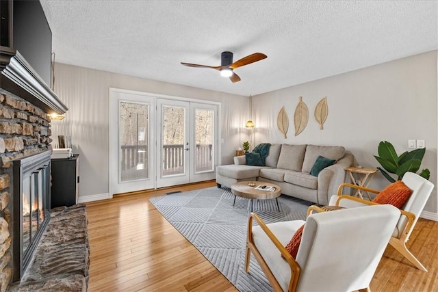 living room featuring french doors, a textured ceiling, ceiling fan, wood-type flooring, and a stone fireplace