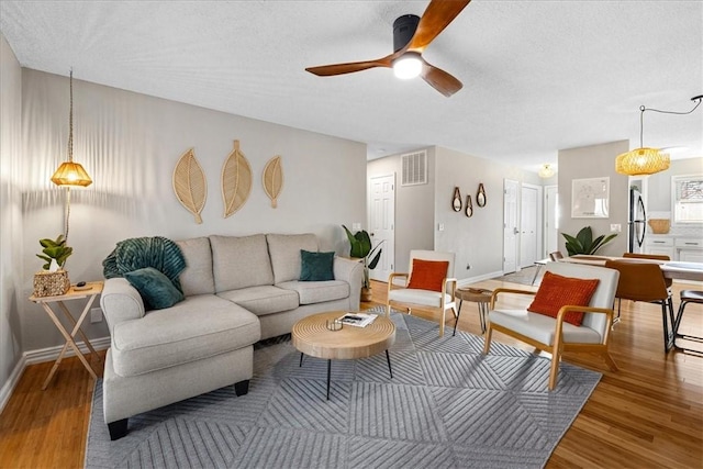 living room featuring ceiling fan, wood-type flooring, and a textured ceiling