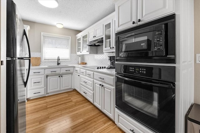 kitchen featuring white cabinetry, sink, light hardwood / wood-style flooring, a textured ceiling, and black appliances