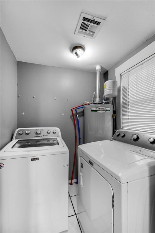 clothes washing area with washer and clothes dryer, light tile patterned floors, and gas water heater