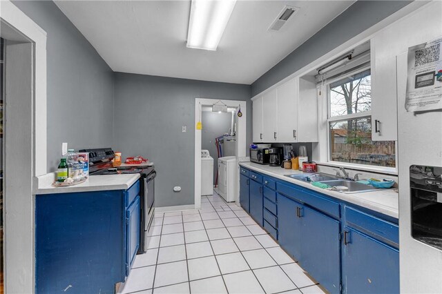 kitchen with electric stove, sink, washer and dryer, blue cabinetry, and white cabinetry