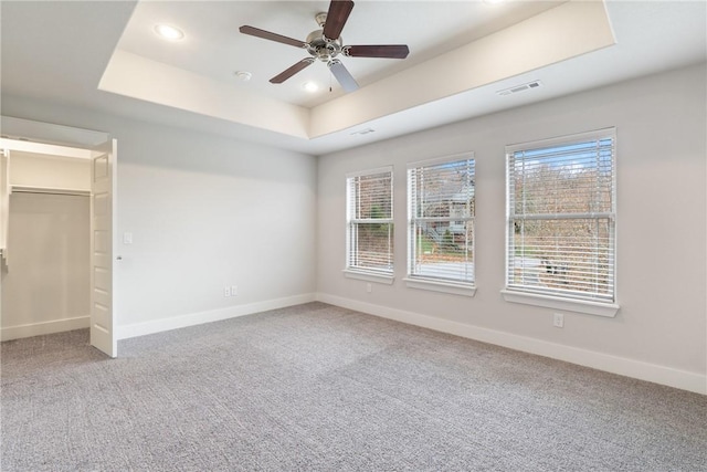 unfurnished bedroom with a closet, carpet floors, a tray ceiling, and ceiling fan