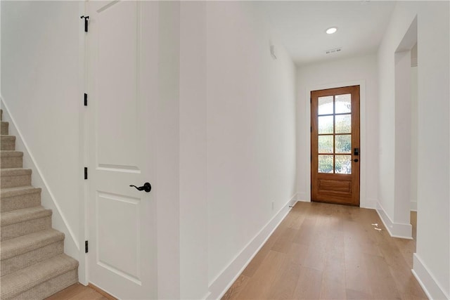 doorway with light wood-type flooring, visible vents, baseboards, and stairs