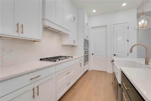 kitchen with a sink, stainless steel appliances, light wood finished floors, and white cabinetry