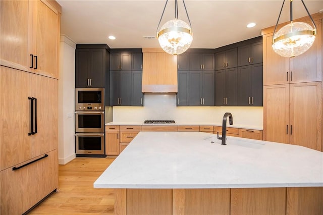 kitchen with light brown cabinets, sink, an island with sink, and hanging light fixtures