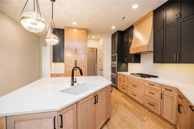 kitchen featuring light brown cabinets, a kitchen island with sink, sink, hanging light fixtures, and light hardwood / wood-style floors