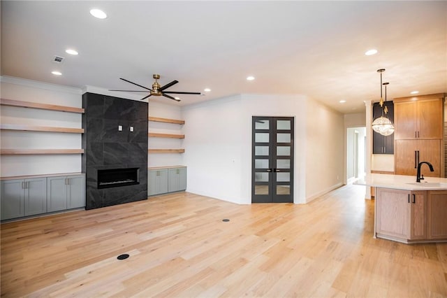 unfurnished living room featuring ceiling fan, sink, light hardwood / wood-style flooring, a high end fireplace, and ornamental molding