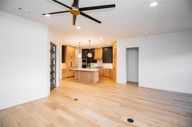 kitchen with pendant lighting, light hardwood / wood-style floors, crown molding, and a kitchen island with sink