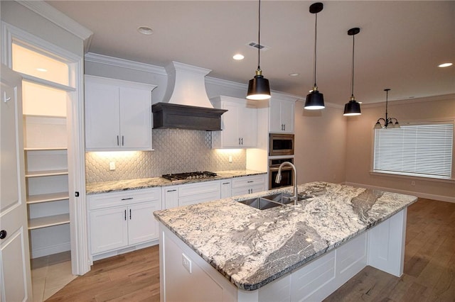 kitchen featuring white cabinets, an island with sink, and custom range hood