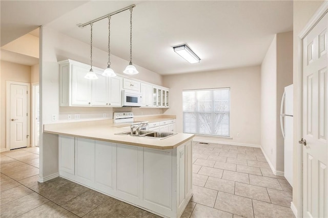 kitchen with kitchen peninsula, white appliances, sink, white cabinets, and hanging light fixtures