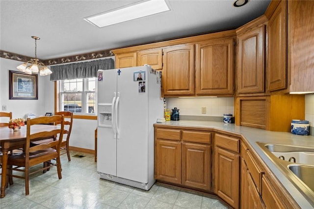 kitchen featuring hanging light fixtures, tasteful backsplash, white fridge with ice dispenser, and sink