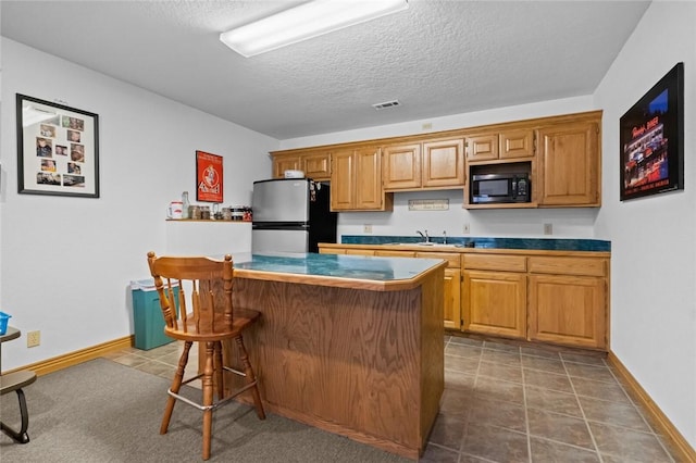 kitchen featuring a kitchen breakfast bar, sink, a textured ceiling, black microwave, and stainless steel refrigerator