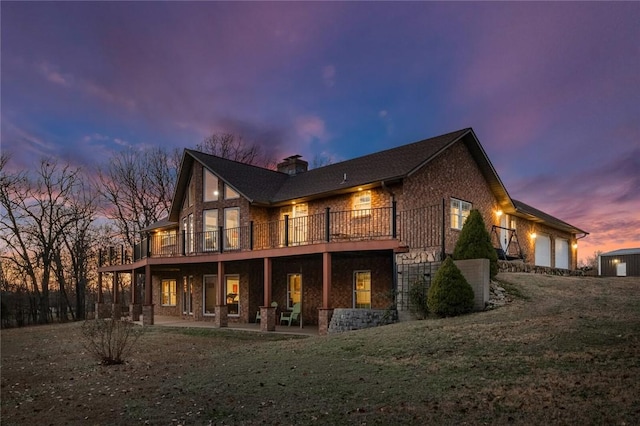 back house at dusk featuring a lawn, a garage, a deck, and a patio