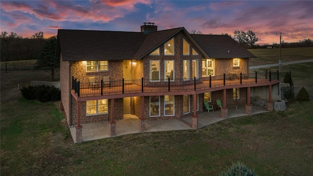 back house at dusk featuring a lawn, a deck, and a patio