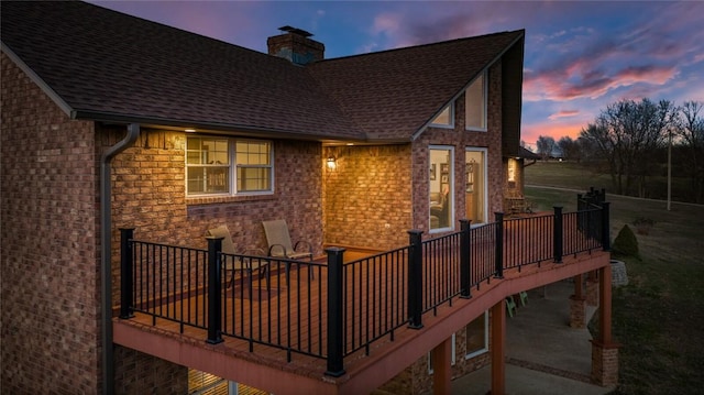 back house at dusk featuring a wooden deck and a patio