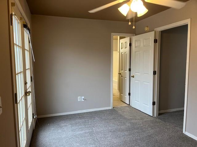 unfurnished room with ceiling fan and dark colored carpet