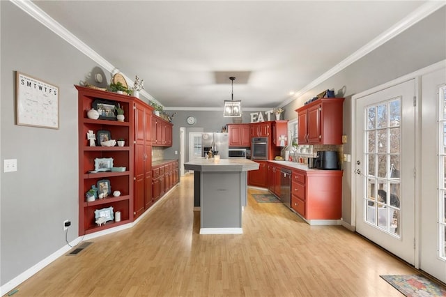 kitchen featuring ornamental molding, stainless steel appliances, decorative light fixtures, light hardwood / wood-style flooring, and a center island