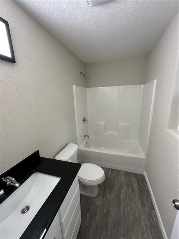 full bathroom with washtub / shower combination, hardwood / wood-style floors, a textured ceiling, toilet, and vanity