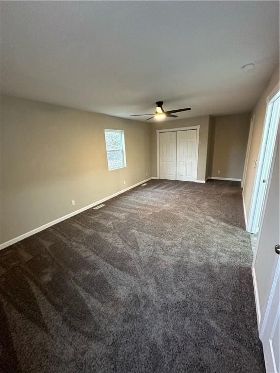 unfurnished bedroom with a closet, dark carpet, and ceiling fan