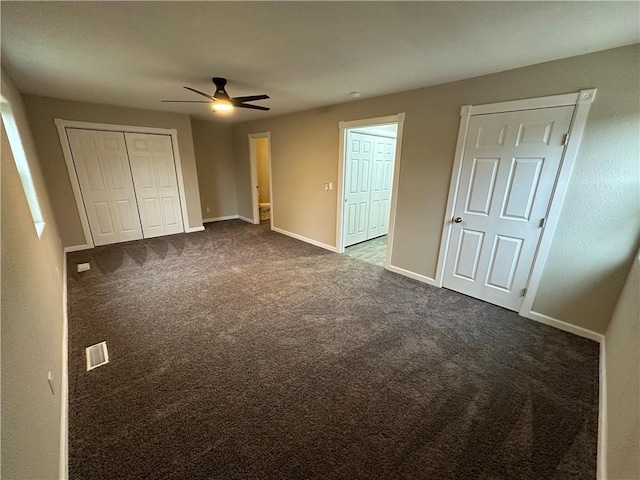 unfurnished bedroom featuring multiple closets, ceiling fan, and dark colored carpet