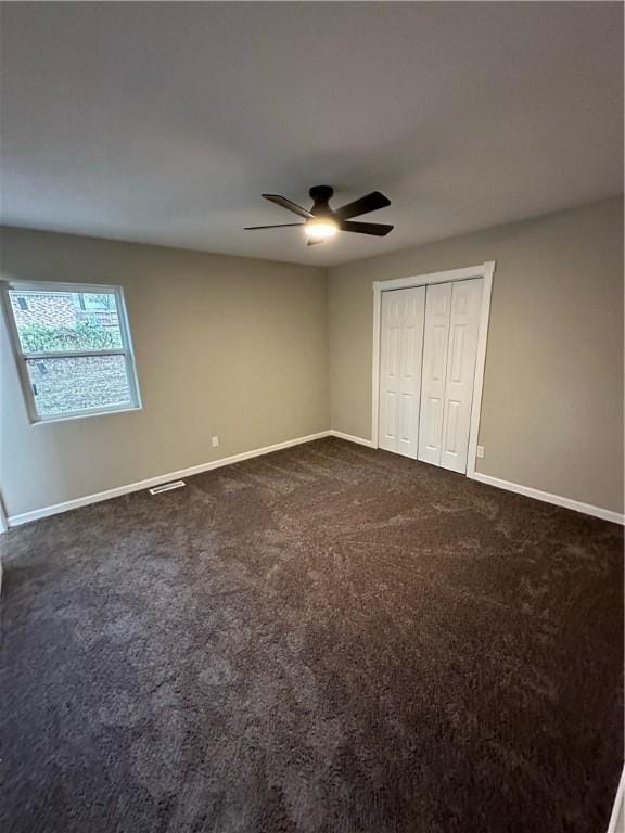 unfurnished bedroom featuring dark colored carpet, a closet, and ceiling fan