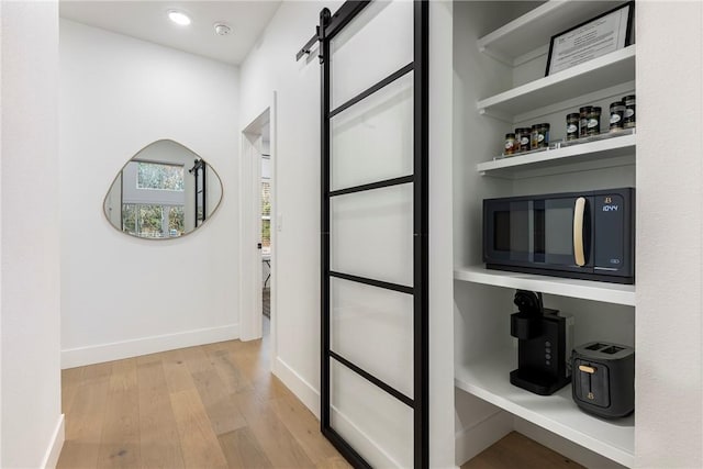 hallway featuring baseboards, light wood-style floors, and a barn door