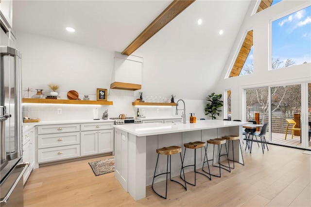 kitchen with light wood finished floors, open shelves, high end fridge, custom range hood, and a kitchen bar