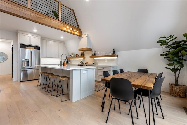 kitchen with a kitchen island with sink, high end fridge, light countertops, light wood-style floors, and a kitchen breakfast bar