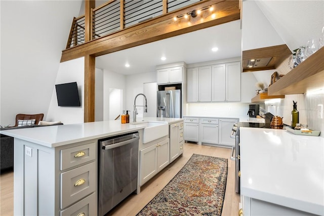 kitchen featuring open shelves, an island with sink, a sink, stainless steel appliances, and light countertops