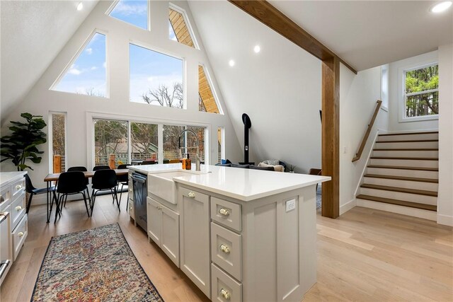 kitchen with dishwasher, a center island with sink, sink, light wood-type flooring, and high vaulted ceiling