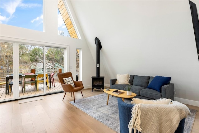 living room featuring light wood-type flooring, baseboards, a towering ceiling, and a wood stove