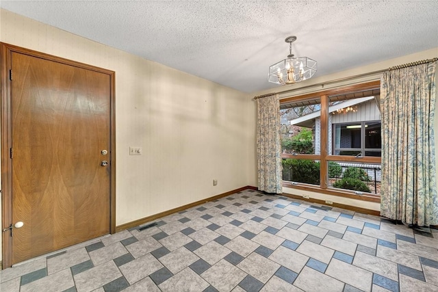 unfurnished room featuring a textured ceiling and a notable chandelier